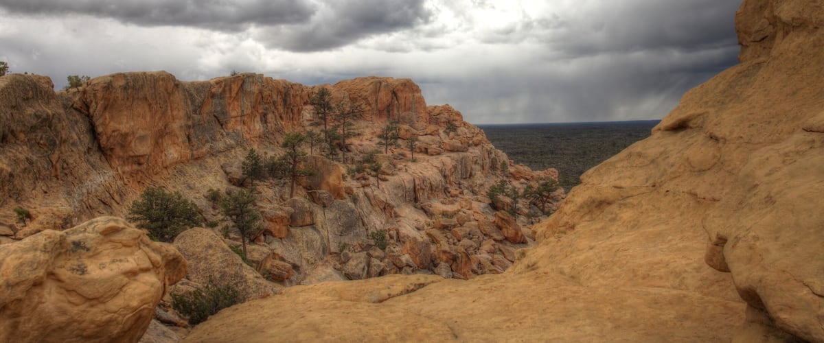 A rugged desert landscape with rocky formations and sparse vegetation under a cloudy sky.
