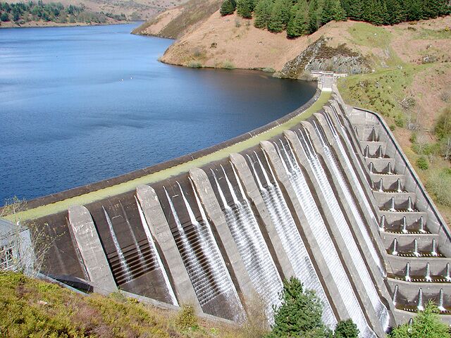 Una gran presa con múltiples vertederos, un lago tranquilo y colinas circundantes.