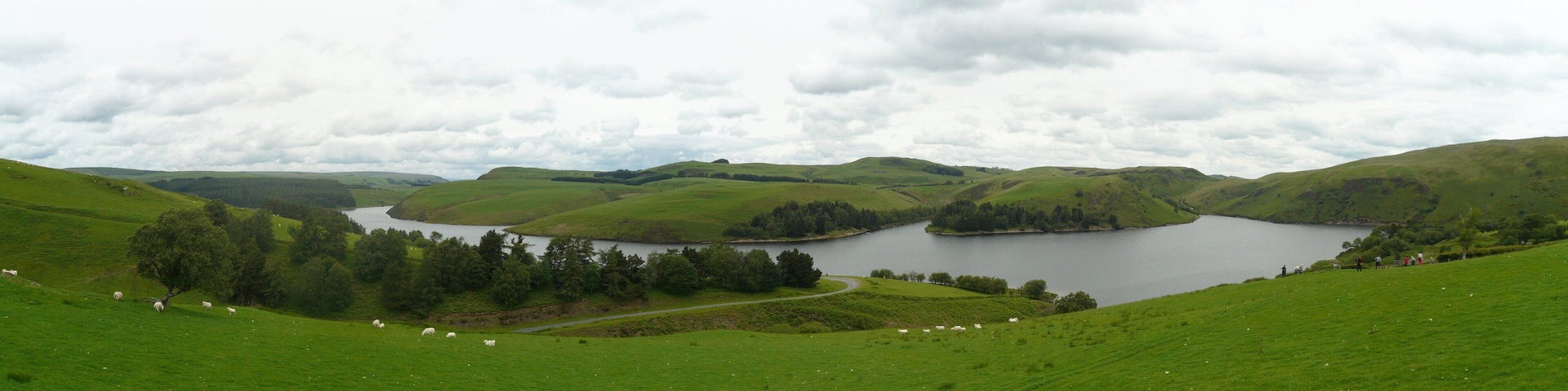 A lake surrounded by rolling green hills and a cloudy sky.