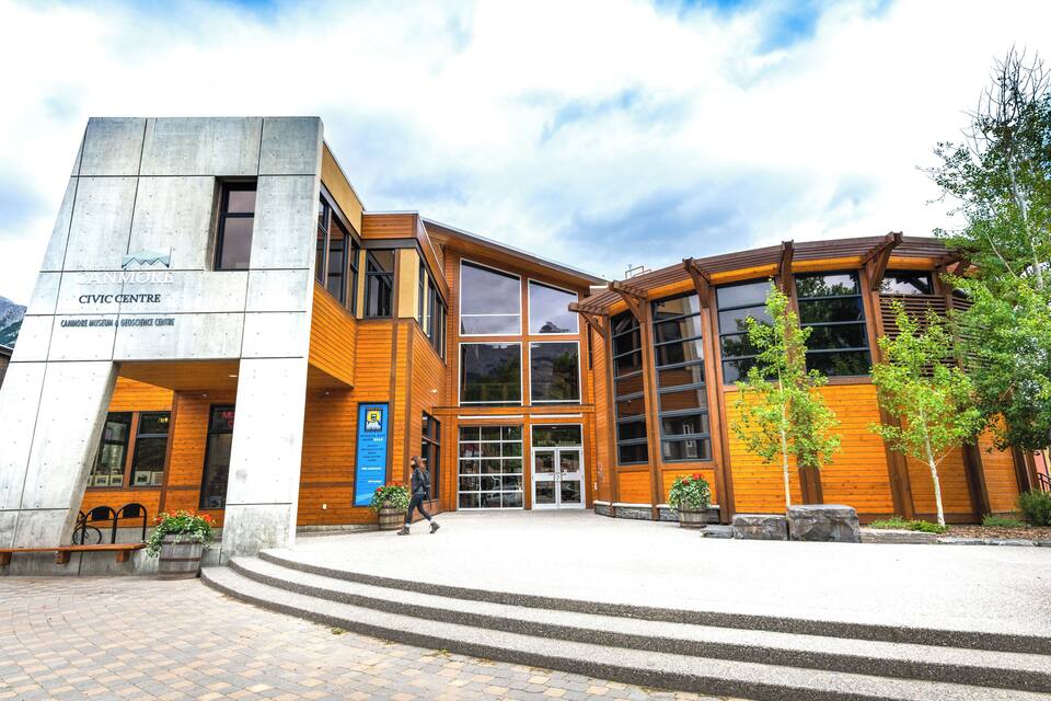 A modern building with a mix of concrete and wood exterior, featuring large windows and a welcoming entrance.