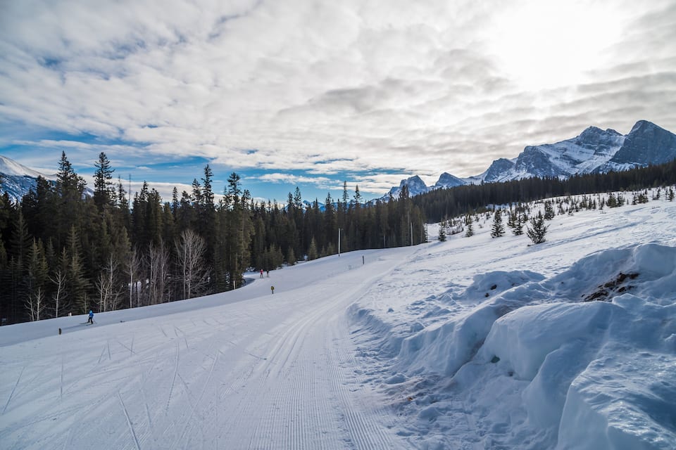 A snowy ski slope with trees and mountains in the background.
