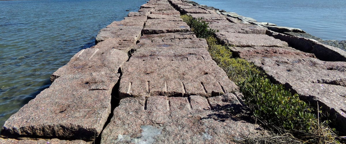 A long, narrow stone pier extending into calm waters, with a clear sky above.