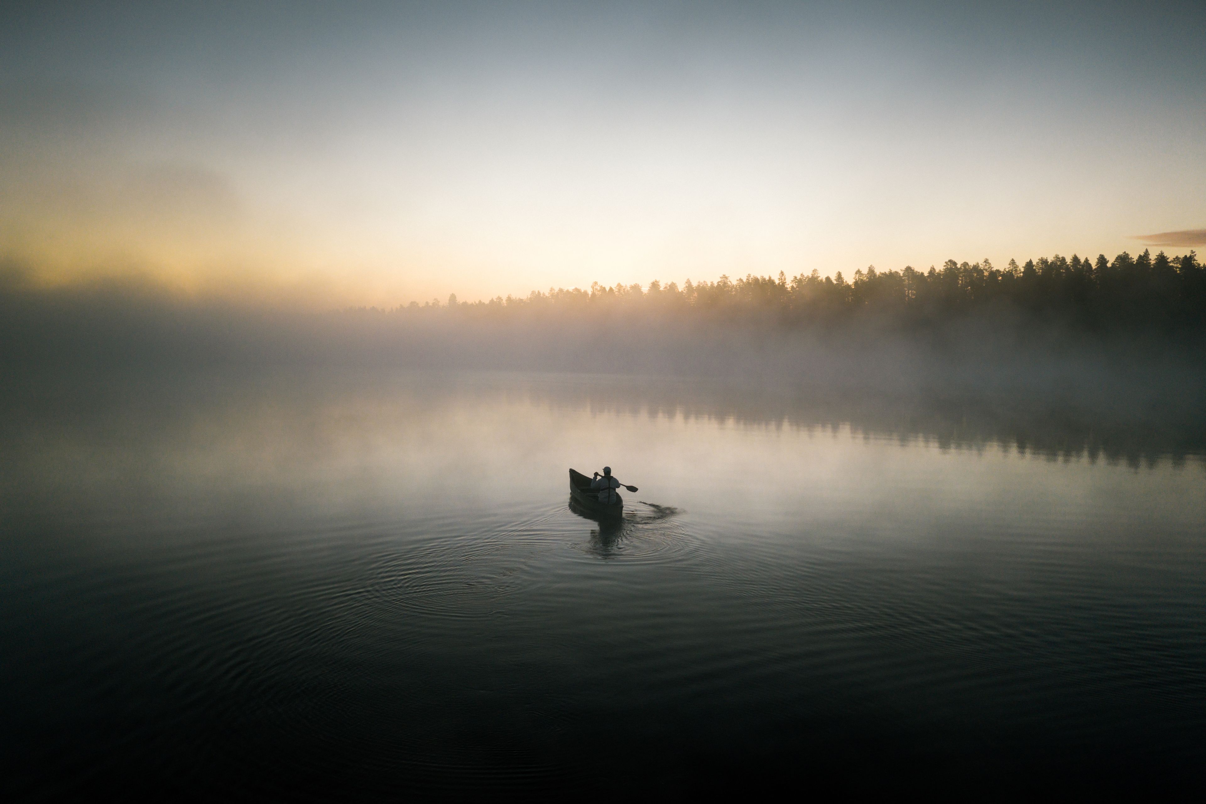 A calm lake with a single boat and a forest in the background.