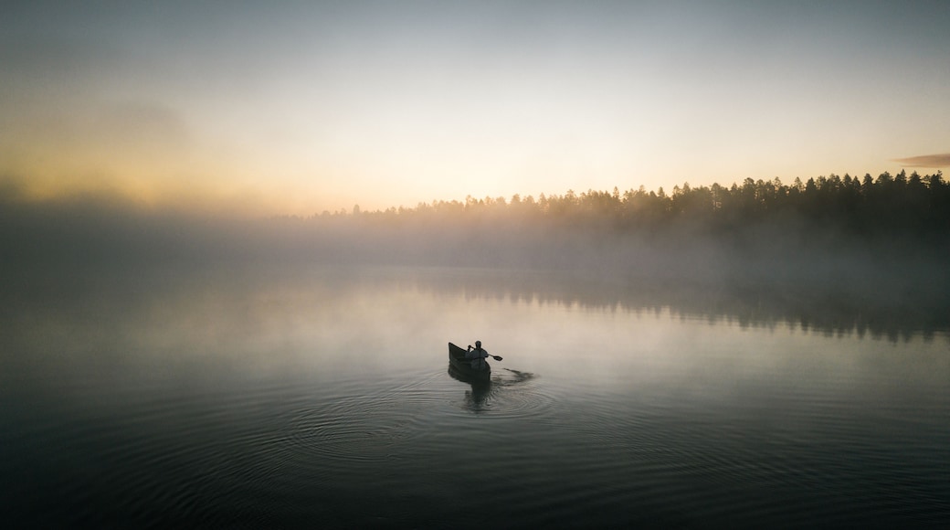 Un lago tranquilo con una sola embarcación y un bosque al fondo.
