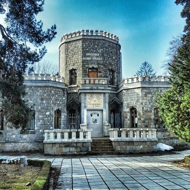 A stone castle with a round tower, a large wooden door, and a stone pathway leading to the entrance.