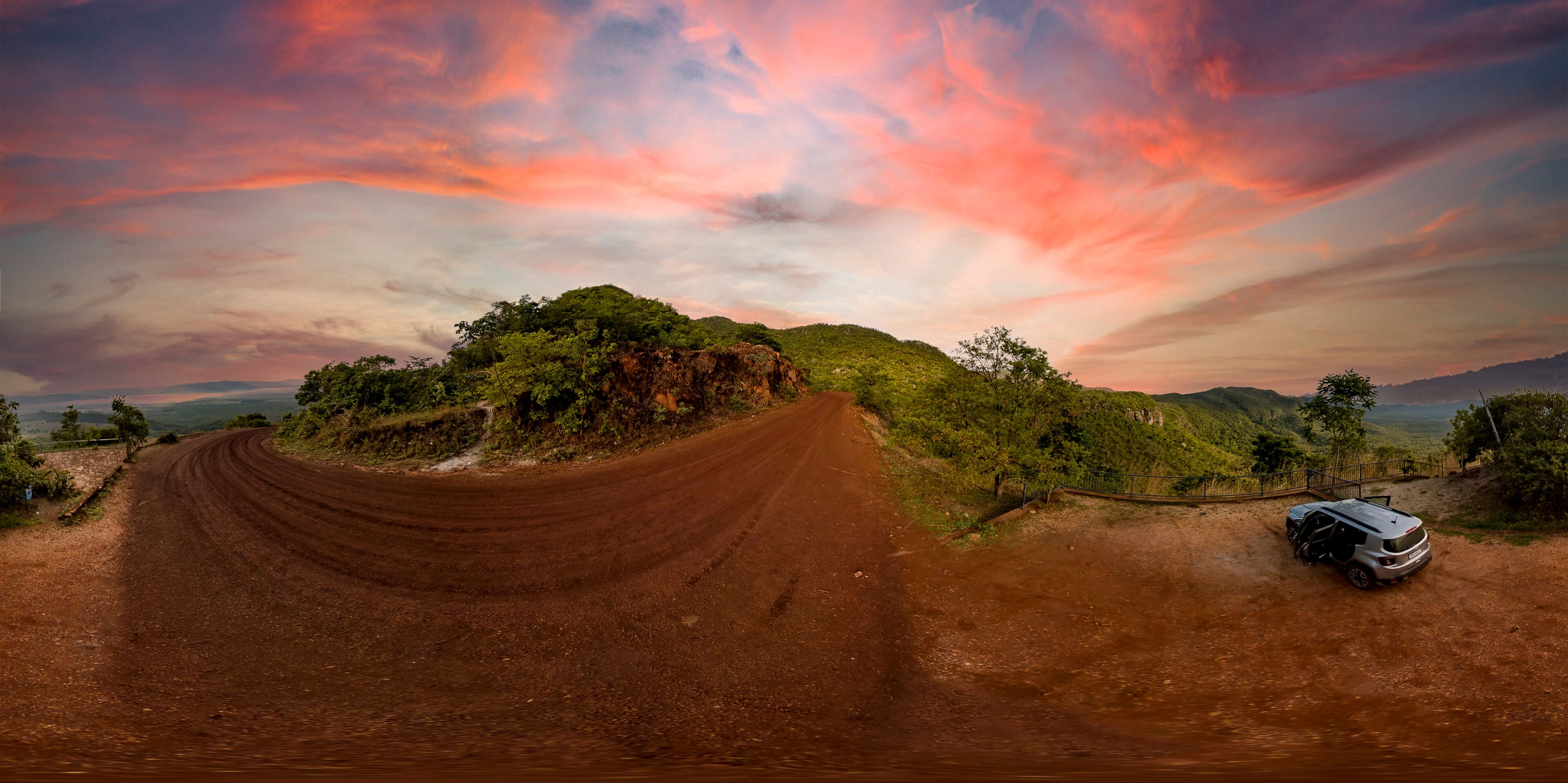 A dirt road curving through a hilly landscape with a car parked on the side.