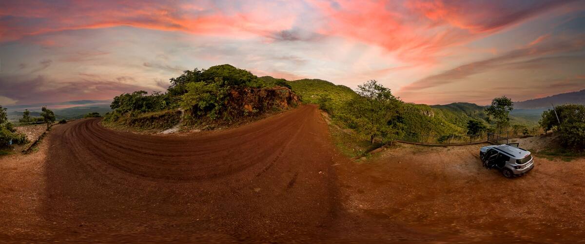 A dirt road curving through a hilly landscape with a car parked on the side.