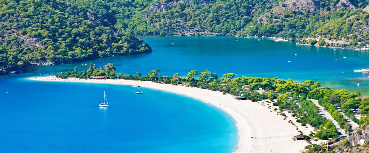 A coastal landscape with a sandy beach, clear turquoise waters, and lush green hills.