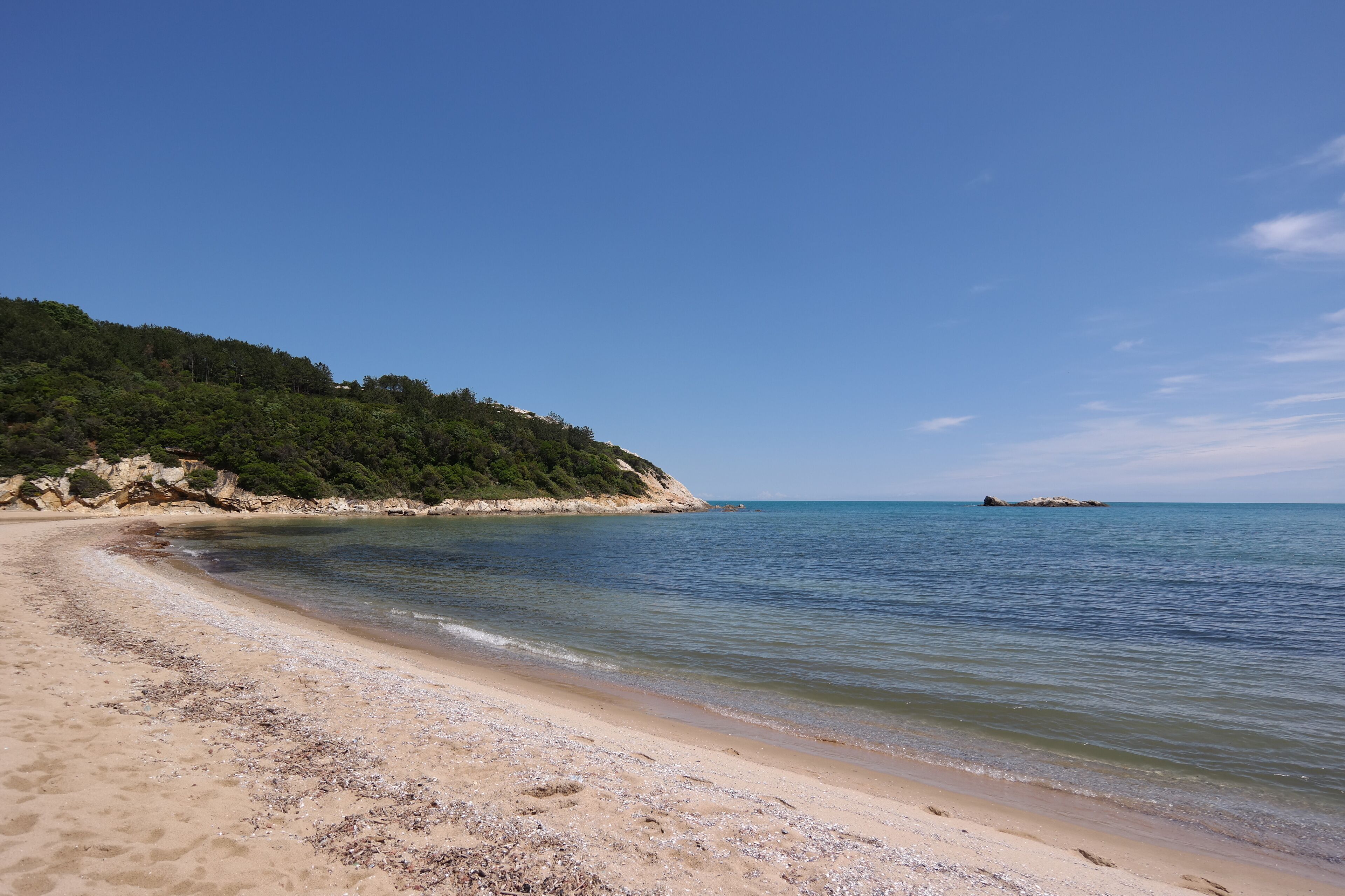 A sandy beach with clear blue water, a rocky outcrop, and a distant island.