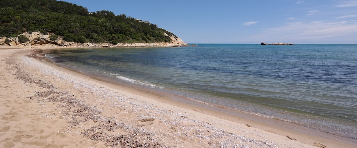 A sandy beach with clear blue water, a rocky outcrop, and a distant island.