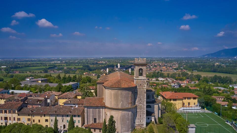 A historic church with a bell tower and dome, surrounded by a town with a soccer field.