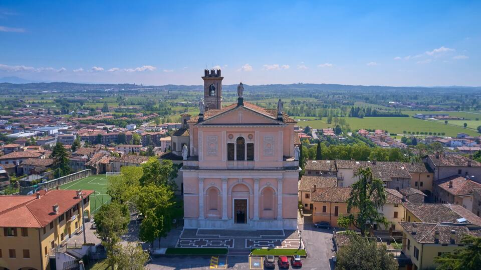 A church with a bell tower, surrounded by a town with green fields and buildings.
