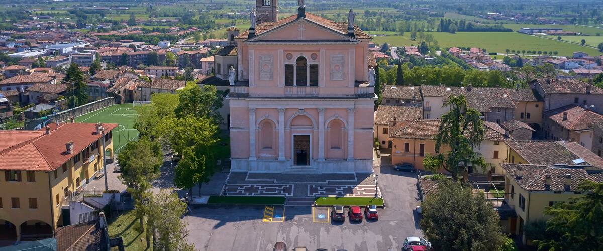 A church with a bell tower, surrounded by a town with green fields and buildings.