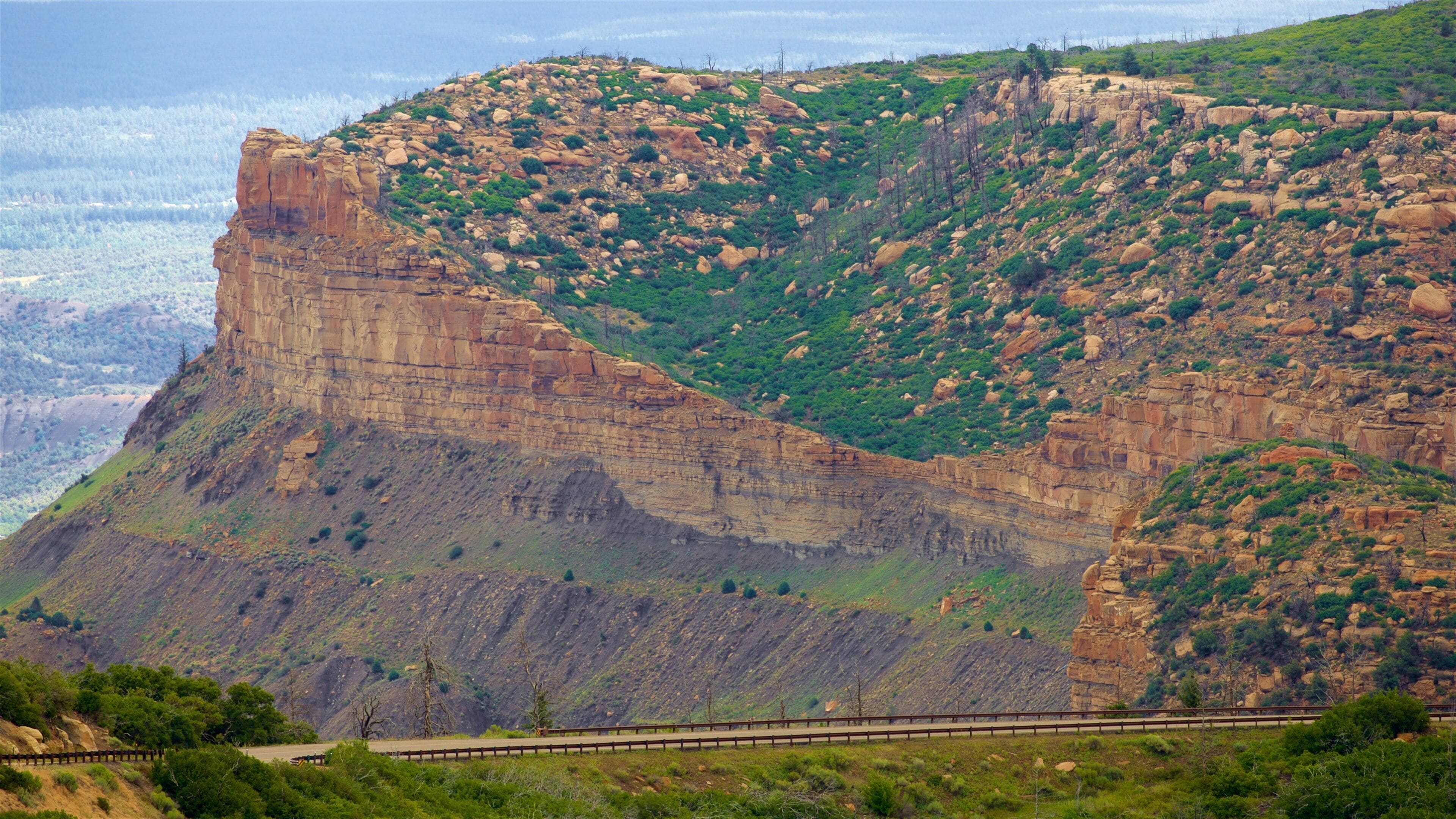 Paisagem montanhosa com uma formação rochosa imponente e uma estrada em primeiro plano.