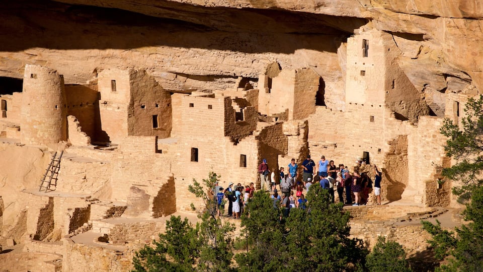 A historic cliffside pueblo with tourists exploring the ruins.