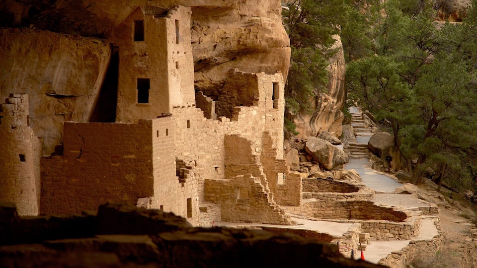 An ancient cliffside pueblo with stone structures and a narrow canyon path.