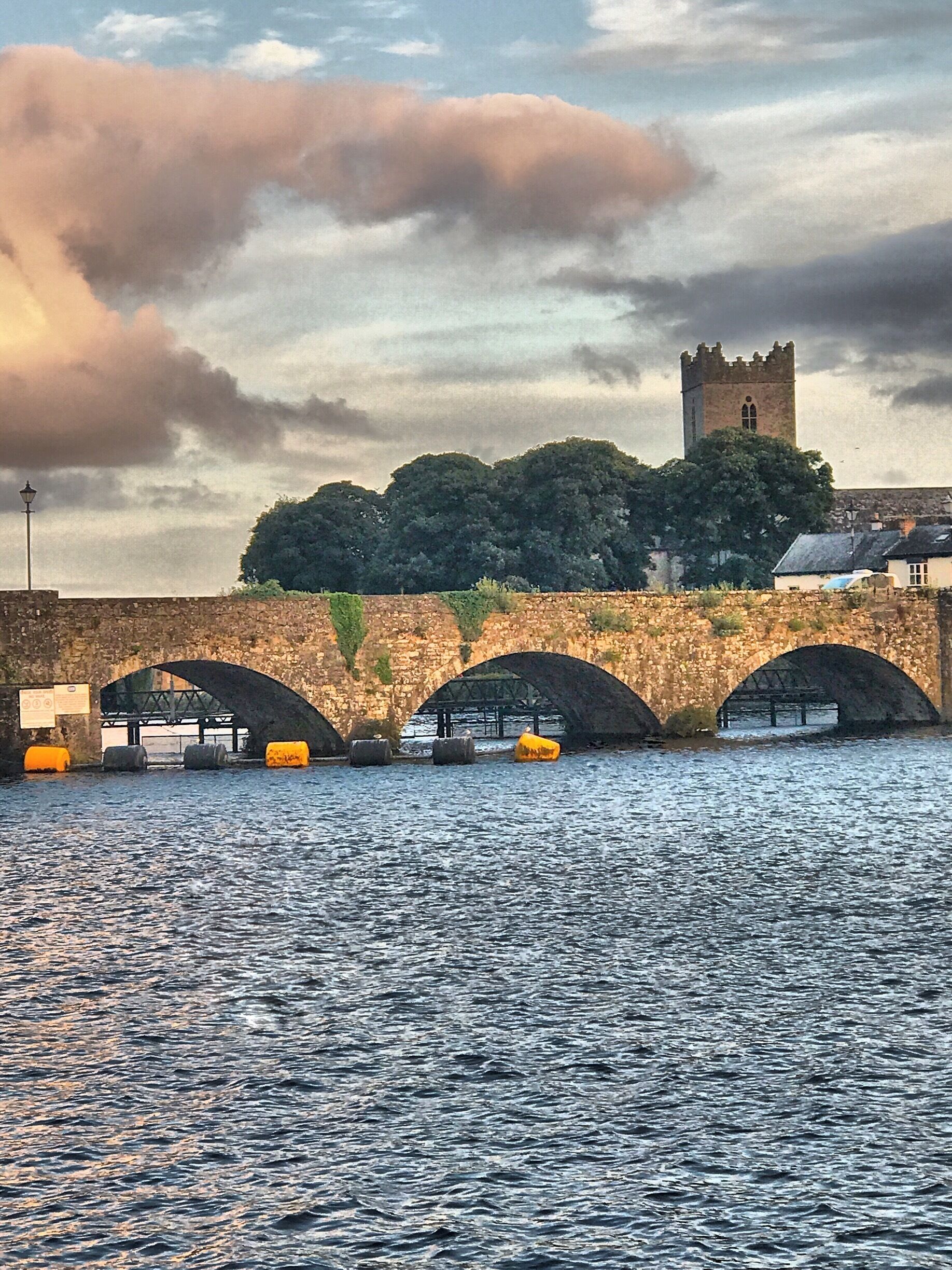 A stone bridge with three arches over a body of water, a tower, and a signboard.