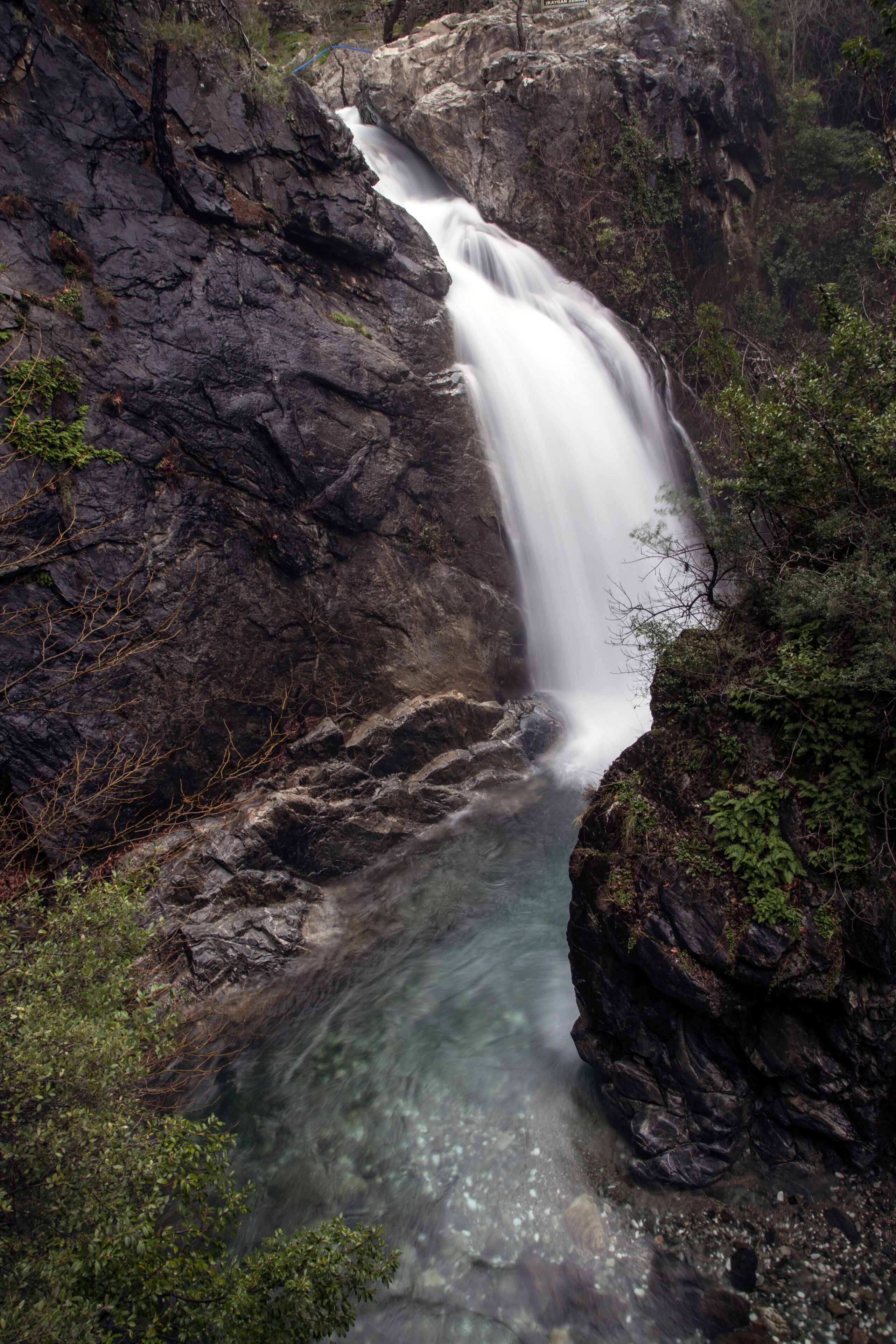 Una cascada que se precipita por un risco rocoso, rodeado de follaje.