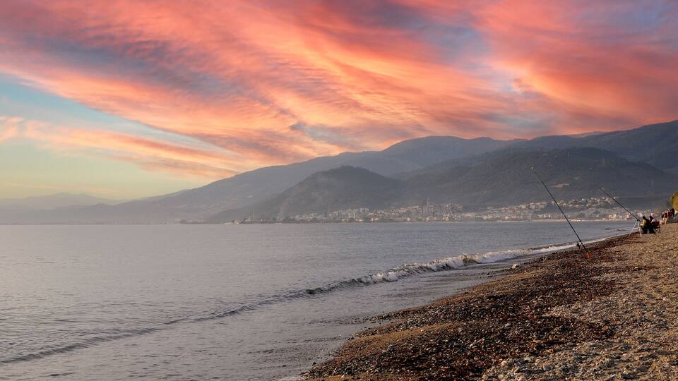 A beach with fishing rods, a rocky shoreline, and mountains in the background.
