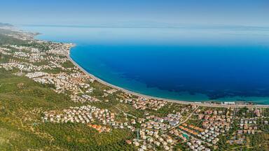 Aerial view of Altinoluk town in Edremit district of Balikesir, Turkey showing coastline, mountains and residential areas on sunny day