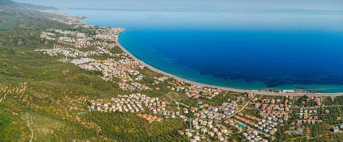 An aerial view of a coastal town with a beach, dense residential area, and surrounding greenery.