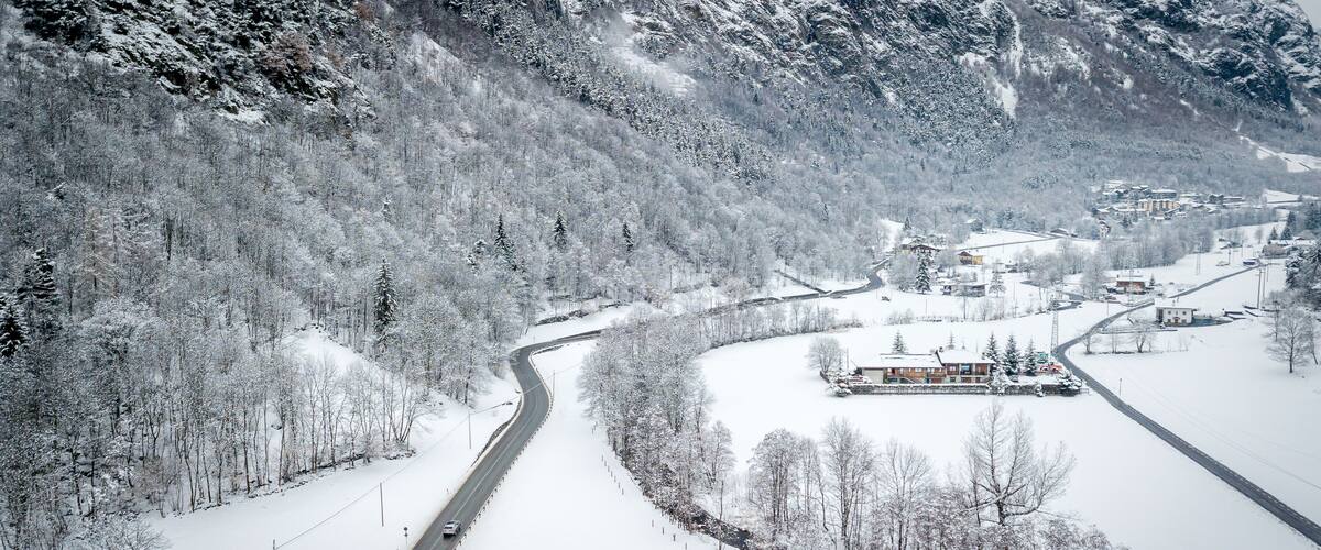 A snow-covered valley with a winding road, a small settlement, and a mountain backdrop.