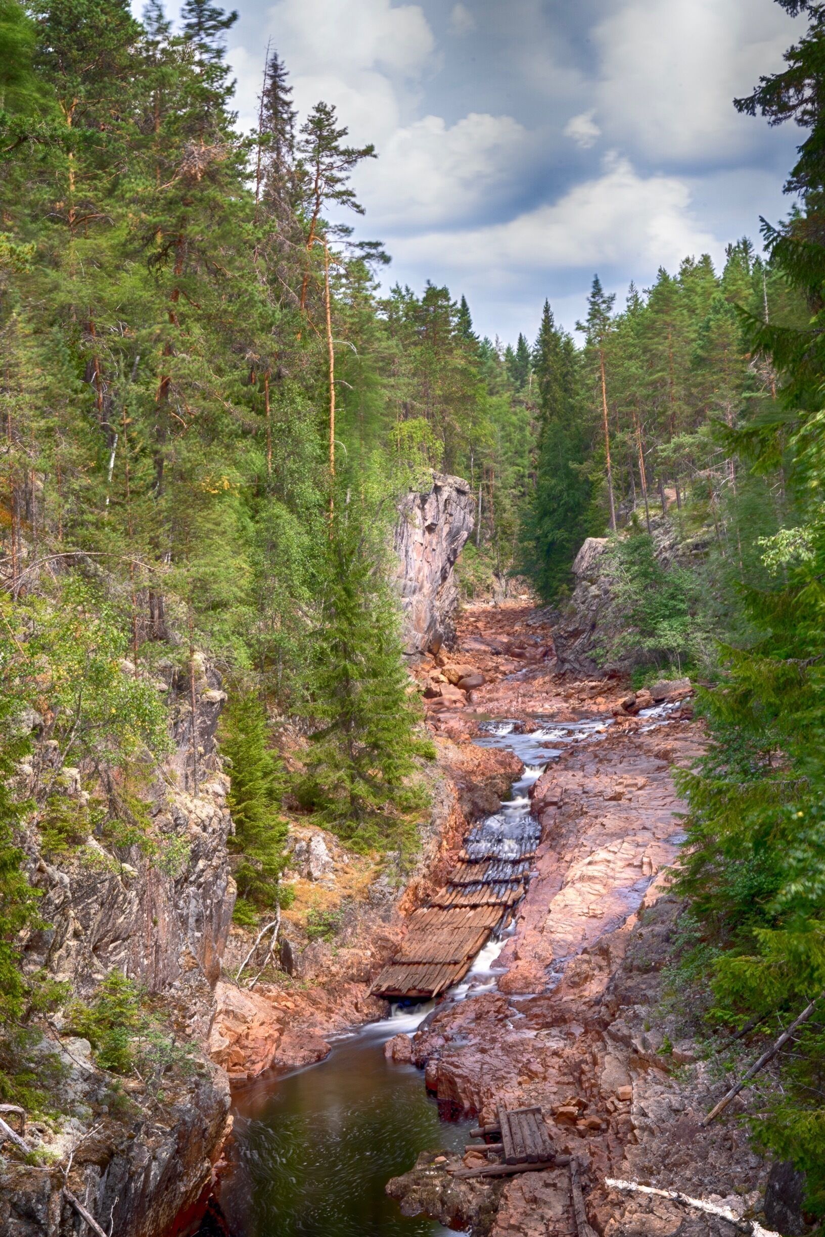 A forested gorge with a flowing river, rocky terrain, and a small traditional hut.
