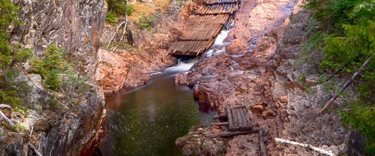 A forested gorge with a flowing river, rocky terrain, and a small traditional hut.