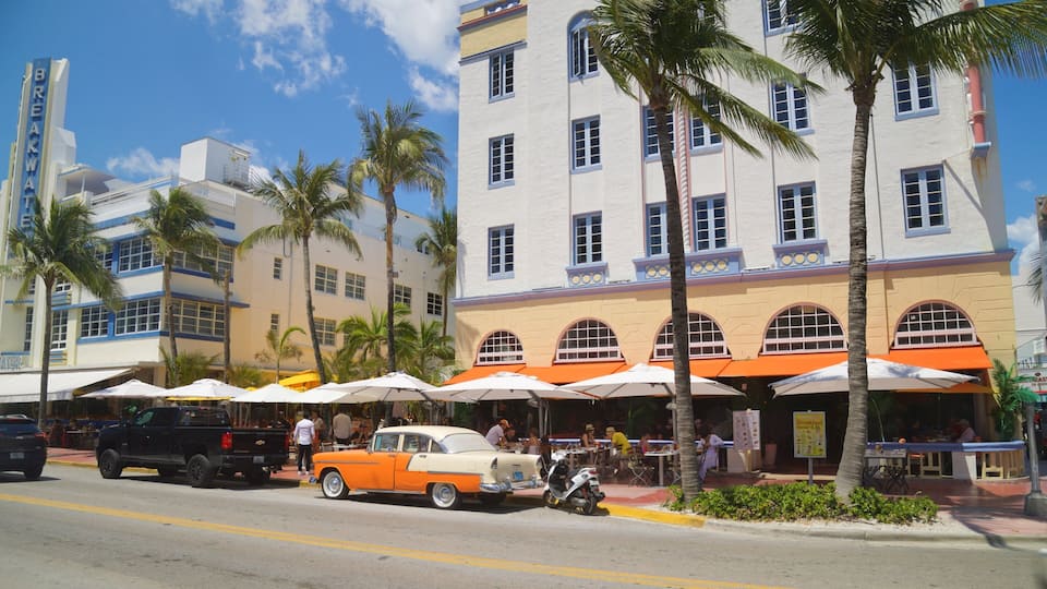 A vintage orange car parked on the street, palm trees, and a white building with blue trim.