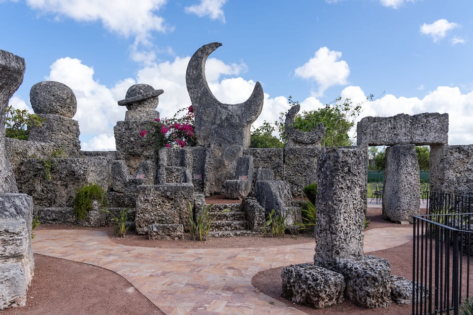 Ancient stone structures with a crescent moon and spherical tops, surrounded by greenery and a clear sky.