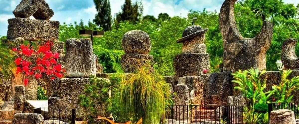 A garden with stone sculptures, red flowers, and lush greenery.