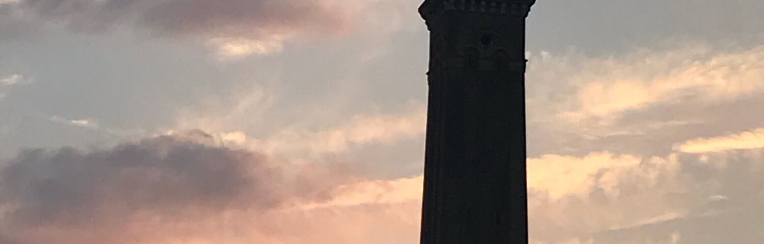 Una torre alta con un veleta en la cima, sobre un cielo de atardecer con nubes.