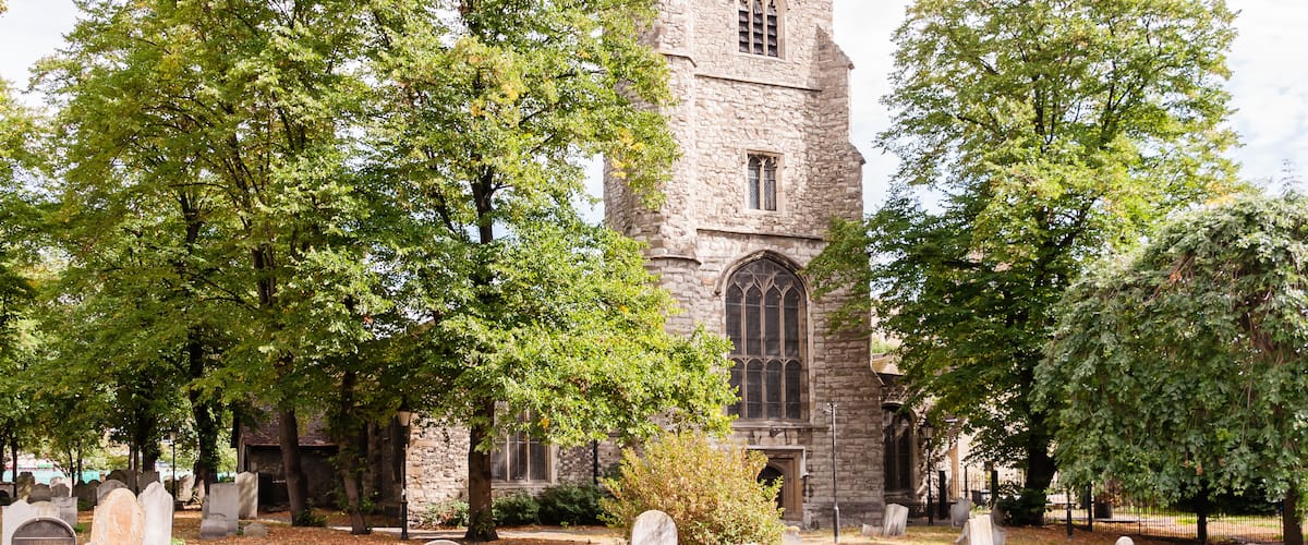 A historic stone church with a tall tower and arched windows, surrounded by mature trees and a cemetery.