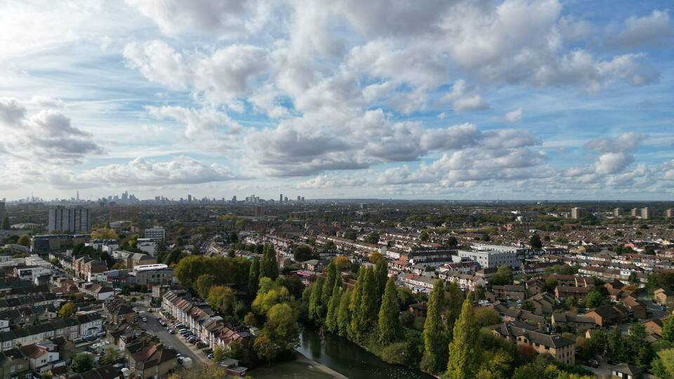 A river winding through a densely populated urban area with a mix of residential and commercial buildings, surrounded by green spaces and trees.