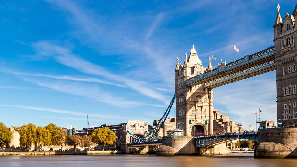 Tower Bridge in London, with the River Thames in the foreground and the Houses of Parliament in the background.