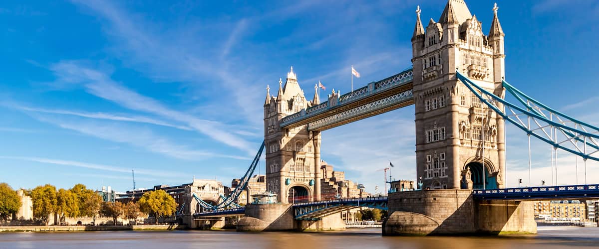 Tower Bridge in London, with the River Thames in the foreground and the Houses of Parliament in the background.