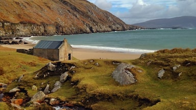 A coastal landscape with a small stone building, rocky terrain, a stream, and a beach.