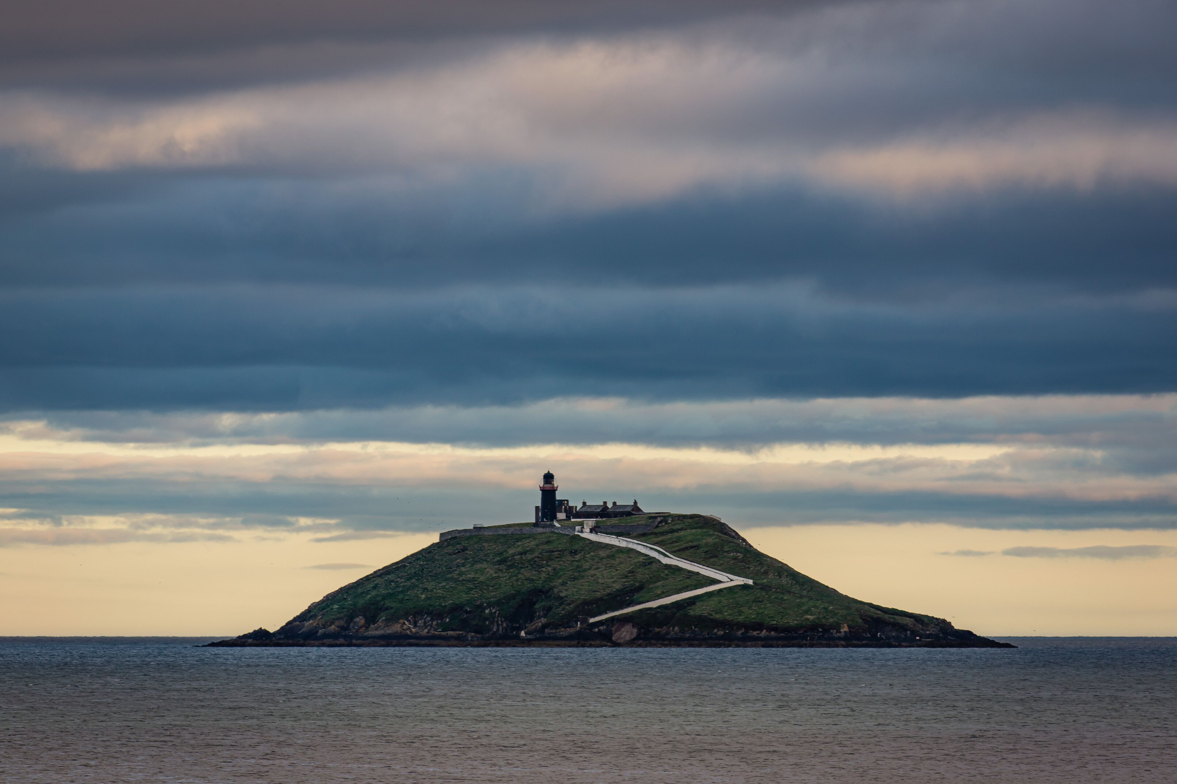 A lighthouse on a grassy hill by the sea under a cloudy sky.