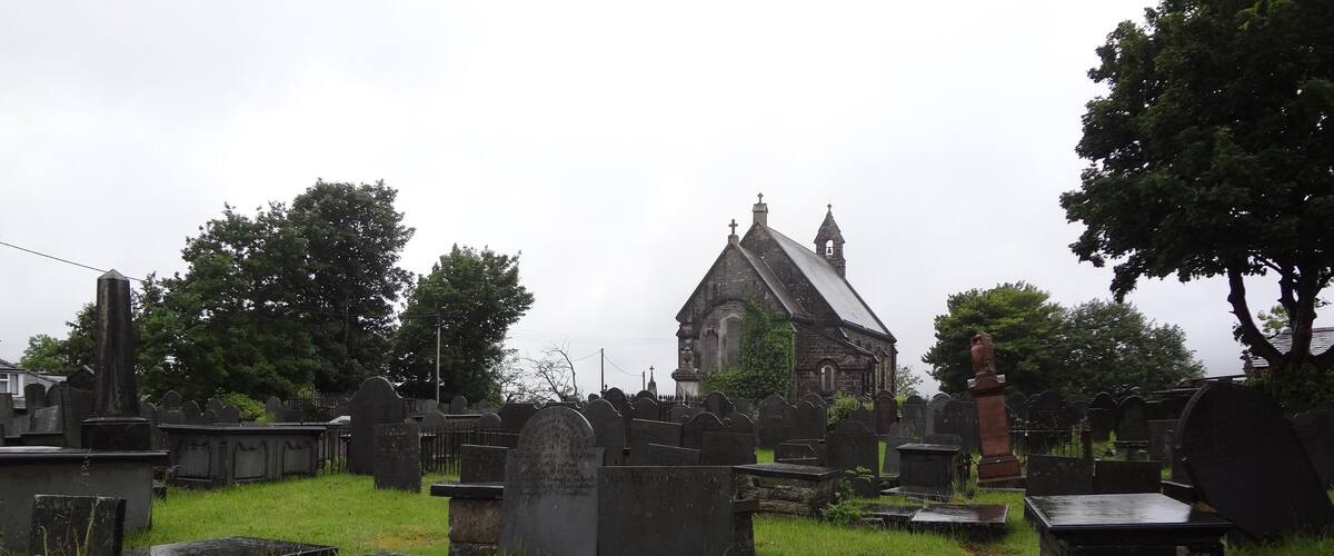 A cemetery with gravestones, a church, and a stone cross.