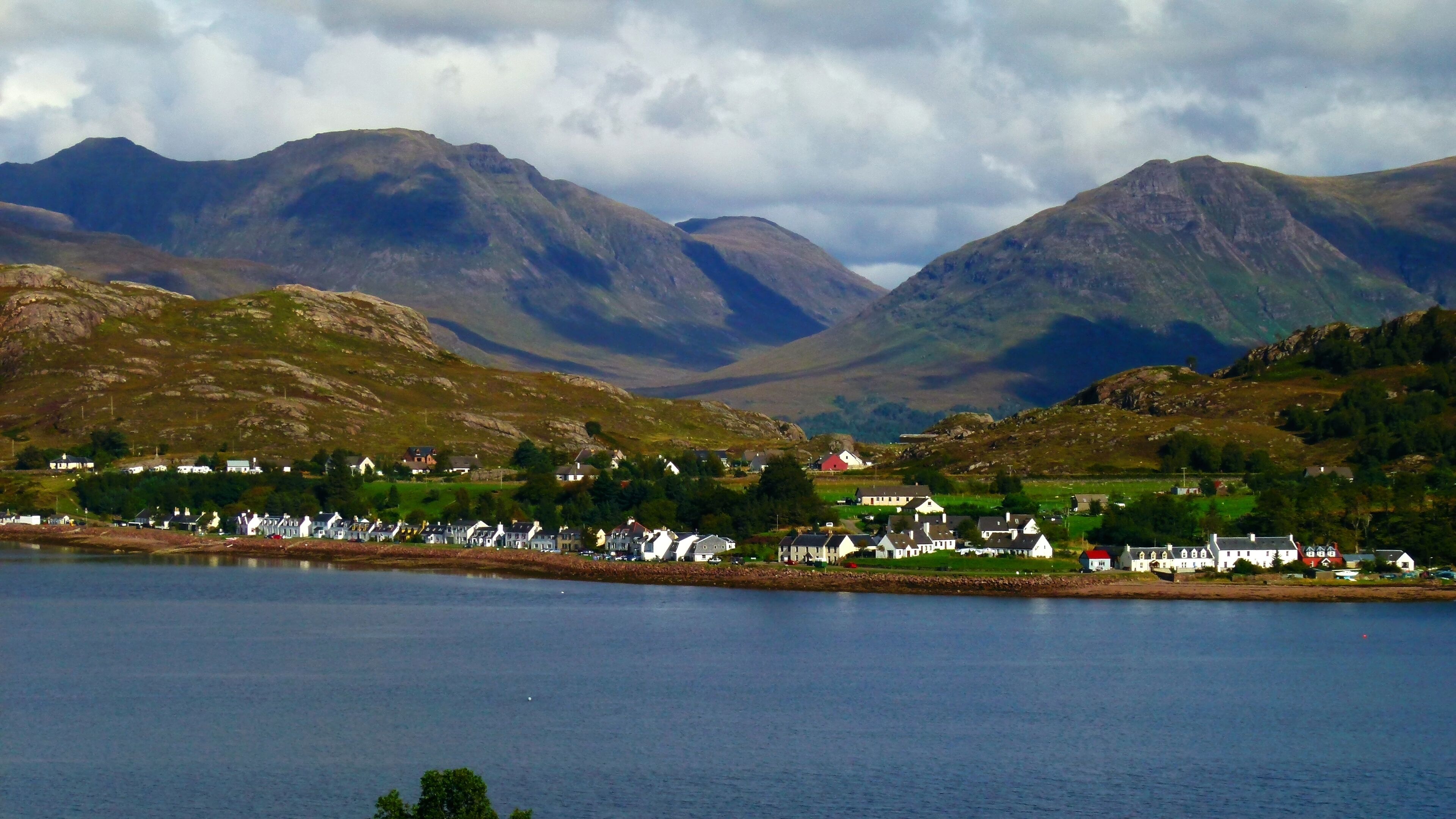 A coastal village with houses along the shoreline, surrounded by mountains and a body of water.