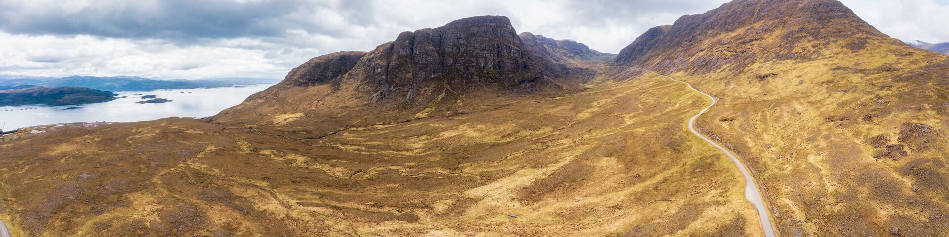 Empty Bealach na Ba road passing through mountains under cloudy sky