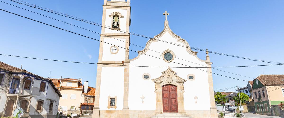 A white church with a bell tower and a red door, surrounded by buildings.
