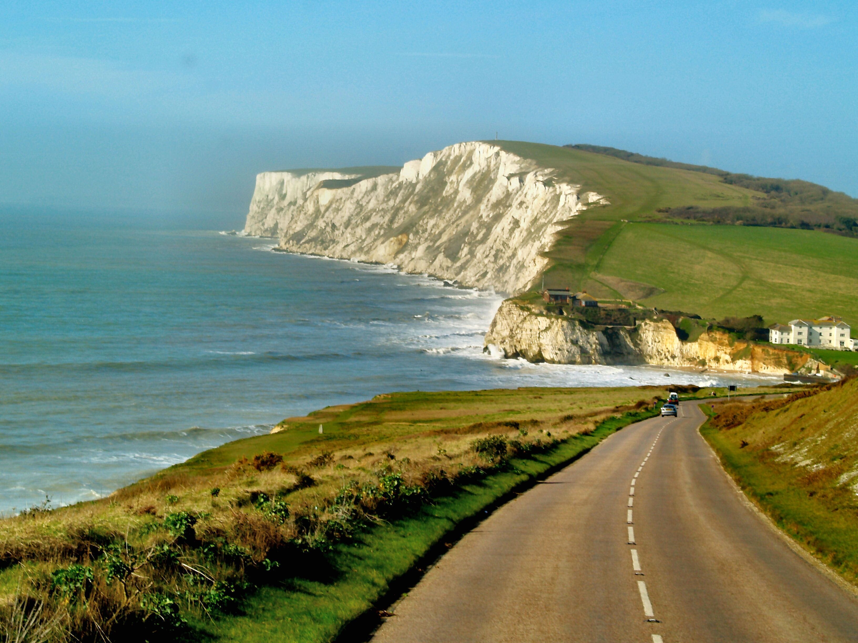 A coastal road with white cliffs, a sea view, and a building on the cliff.