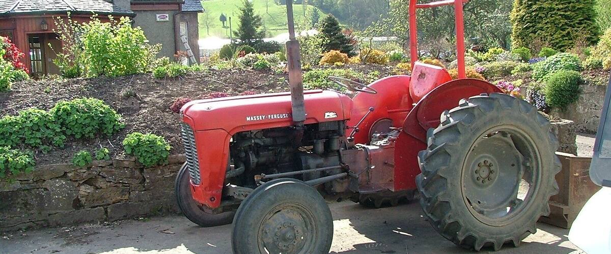 A red Massey Ferguson tractor parked on a rural road with a stone wall and greenery in the background.