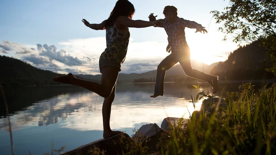 Two people jumping into a lake at sunset with mountains in the background.