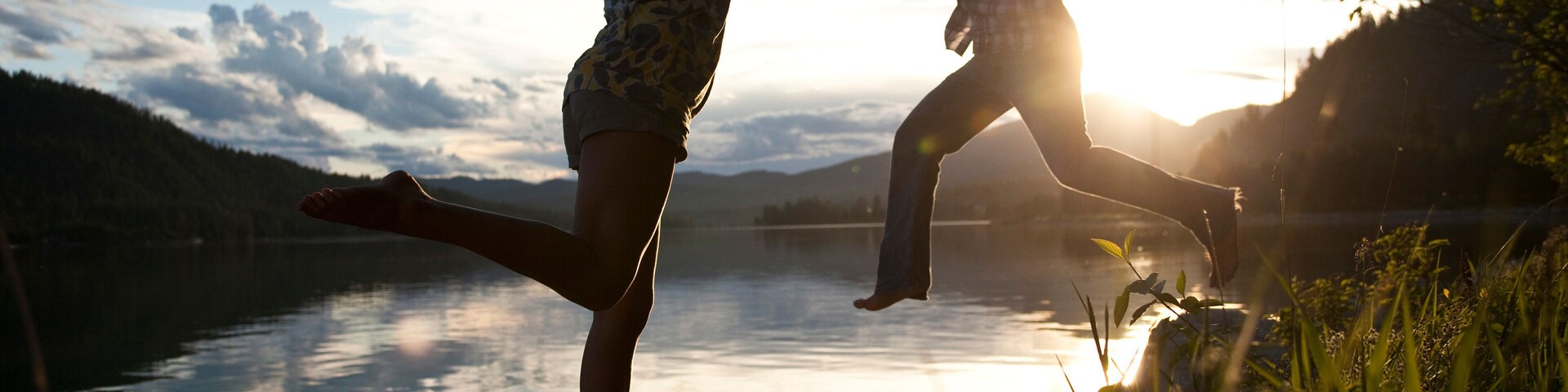 Two young adults balancing on rocks at sunset next to the lake.