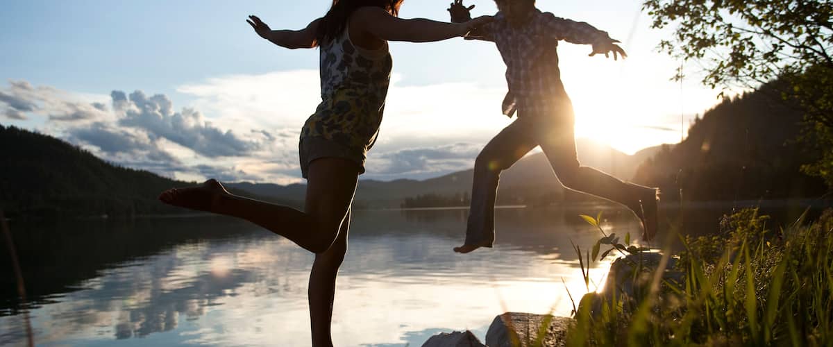 Two people jumping into a lake at sunset with mountains in the background.