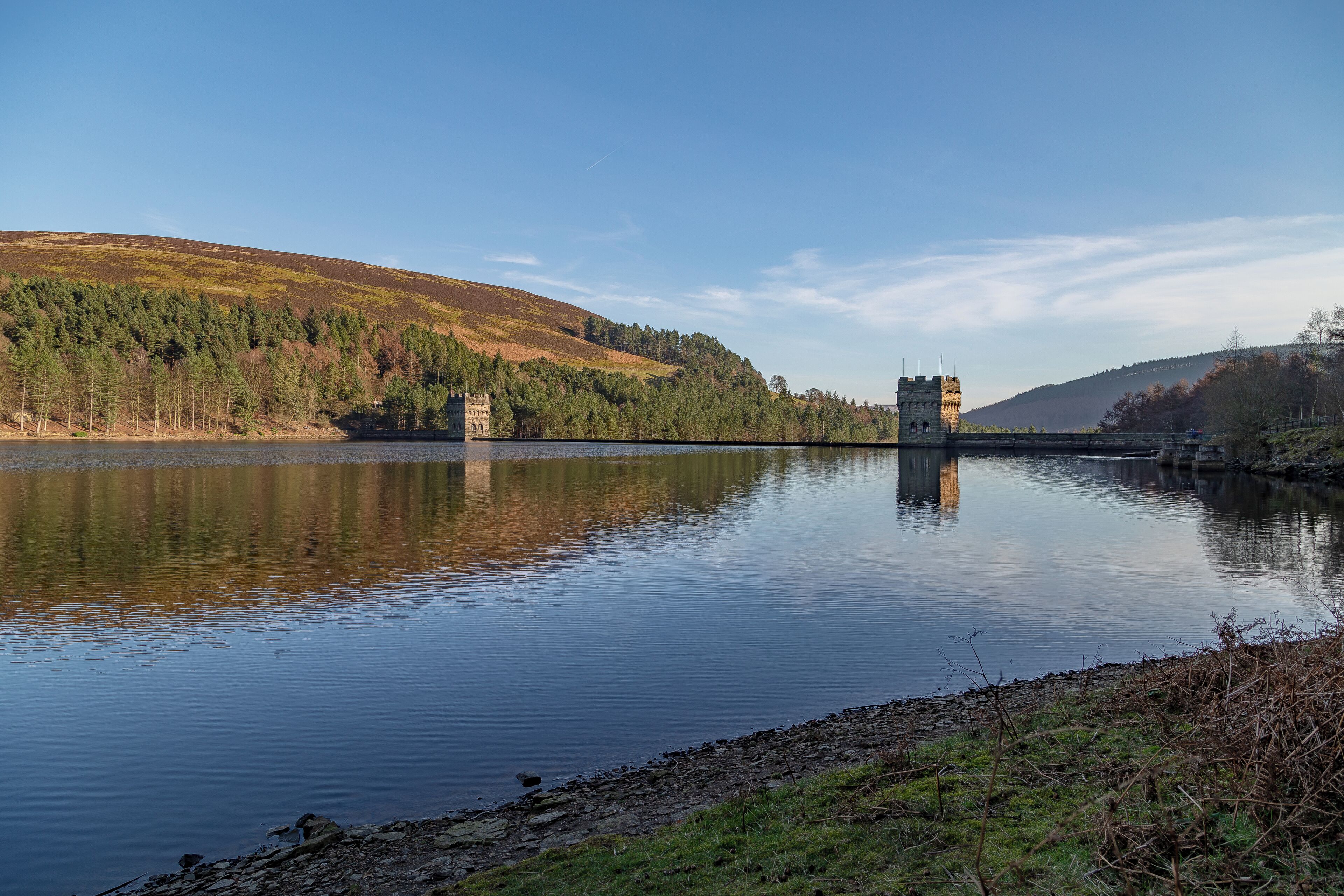 A calm lake with a castle on a hill, surrounded by trees and hills.