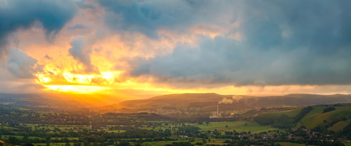 A valley with rolling hills, a distant smokestack, and a sunset.