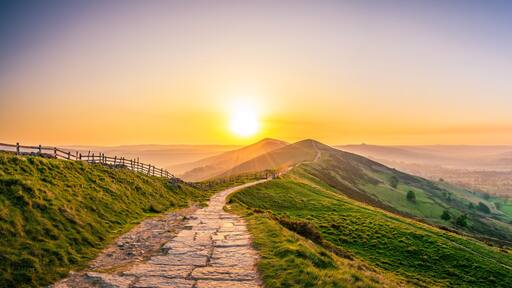 A stone path winding through a valley with a sunset in the background.